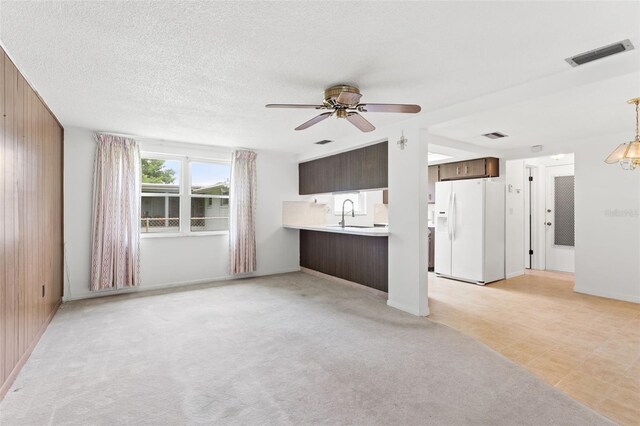 unfurnished living room featuring light carpet, sink, ceiling fan with notable chandelier, and wooden walls