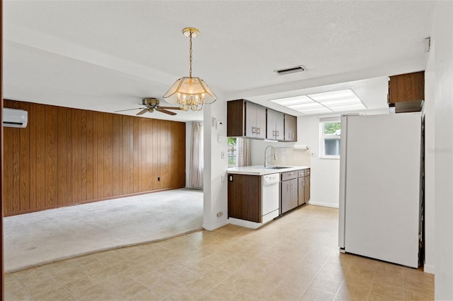 kitchen with sink, white appliances, decorative light fixtures, an AC wall unit, and wood walls