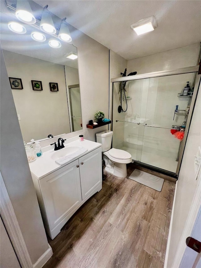 bathroom featuring vanity, a textured ceiling, wood-type flooring, toilet, and walk in shower