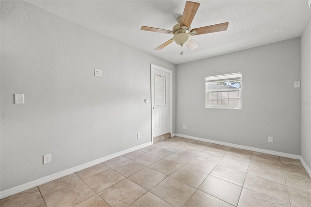 empty room with a ceiling fan, light tile patterned flooring, and baseboards