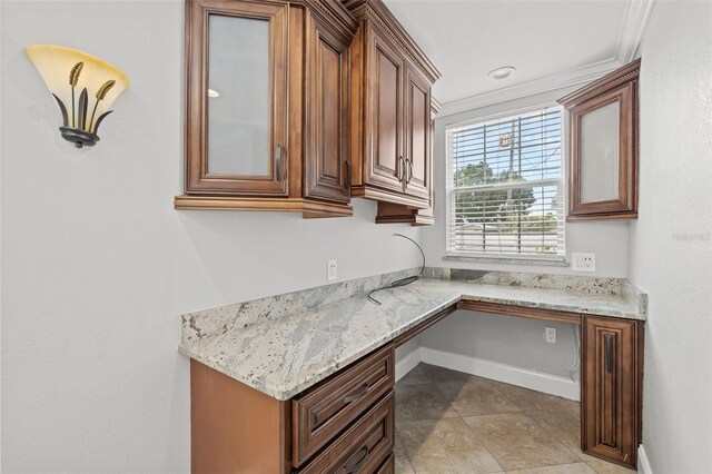 kitchen featuring glass insert cabinets, light stone countertops, baseboards, and built in desk