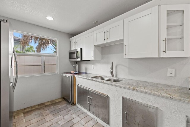 kitchen with a textured ceiling, light stone counters, stainless steel appliances, a sink, and white cabinetry