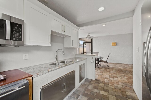 kitchen featuring ceiling fan, light stone counters, stainless steel microwave, white cabinetry, and a sink