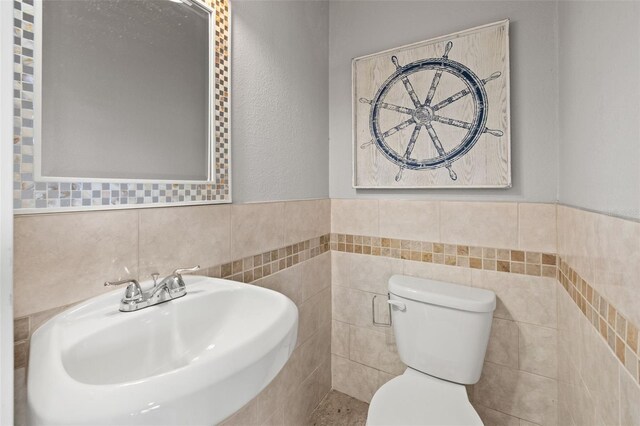 half bath featuring wainscoting, a sink, toilet, and tile walls