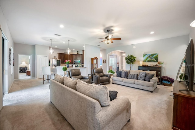 living area with arched walkways, light colored carpet, visible vents, and recessed lighting