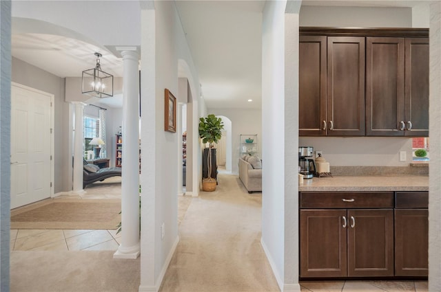 corridor with arched walkways, decorative columns, light tile patterned floors, light colored carpet, and baseboards