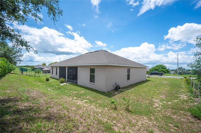 back of house with roof with shingles, fence, a lawn, and stucco siding