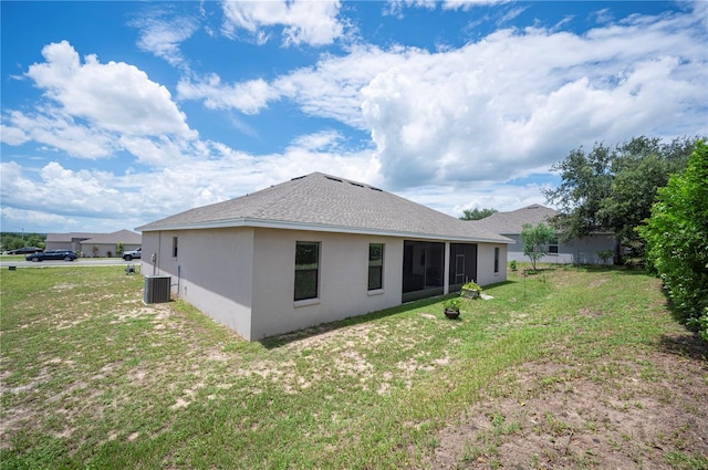 back of property with stucco siding, roof with shingles, central AC, and a yard