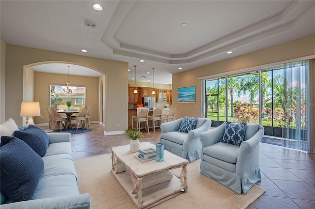 living room featuring a notable chandelier, a tray ceiling, light tile patterned flooring, and a healthy amount of sunlight