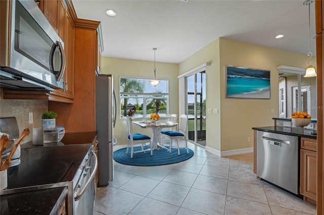 kitchen featuring dark stone countertops, hanging light fixtures, light tile patterned floors, stainless steel appliances, and tasteful backsplash