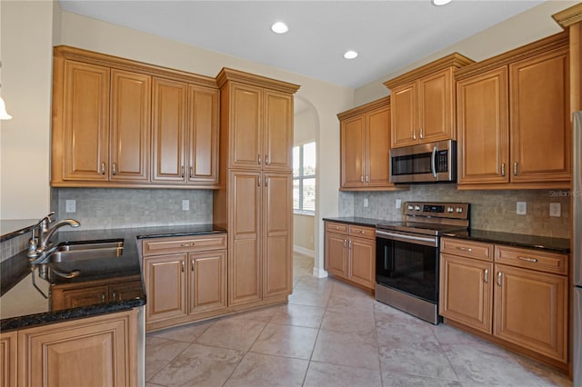 kitchen featuring light tile patterned floors, backsplash, appliances with stainless steel finishes, sink, and dark stone countertops