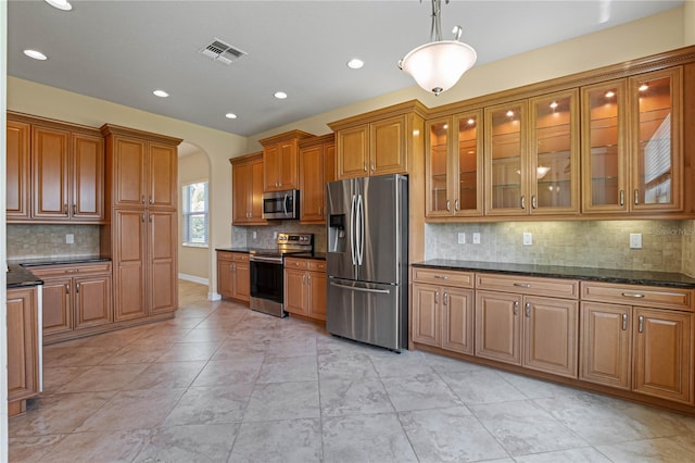 kitchen featuring hanging light fixtures, stainless steel appliances, dark stone counters, and tasteful backsplash