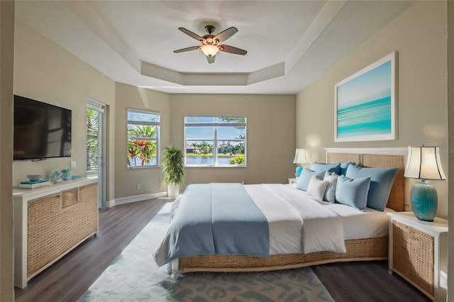 bedroom with dark wood-type flooring, ceiling fan, and a raised ceiling