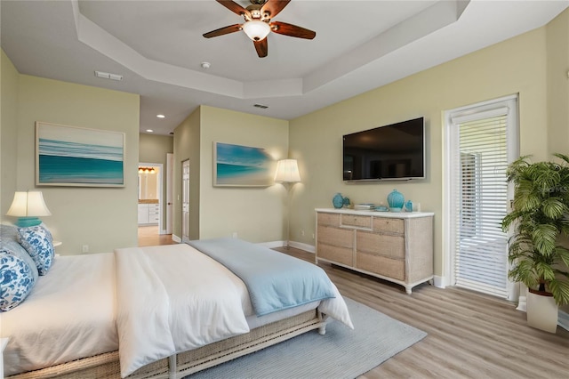 bedroom featuring ceiling fan, hardwood / wood-style floors, ensuite bathroom, and a tray ceiling