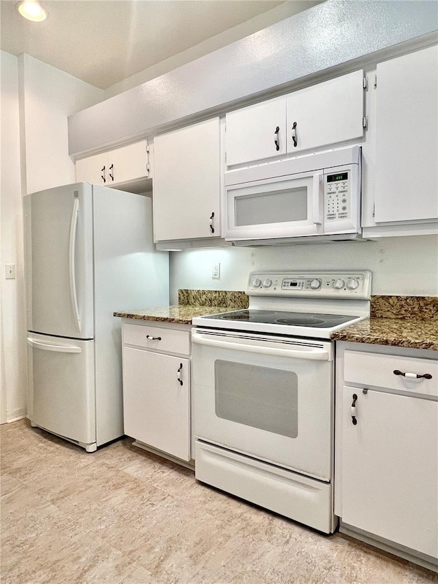 kitchen featuring white appliances, dark stone counters, and white cabinets