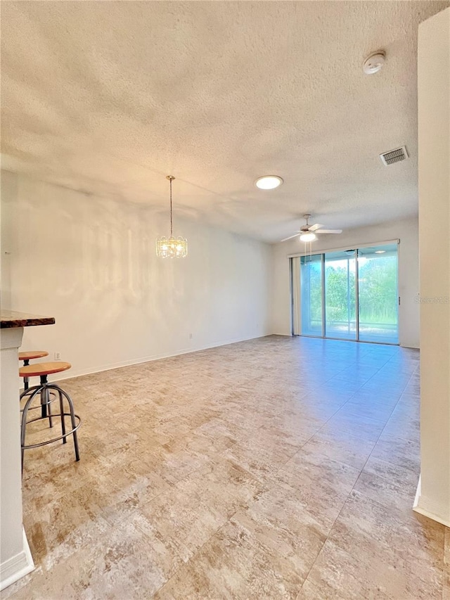 empty room with ceiling fan with notable chandelier and a textured ceiling