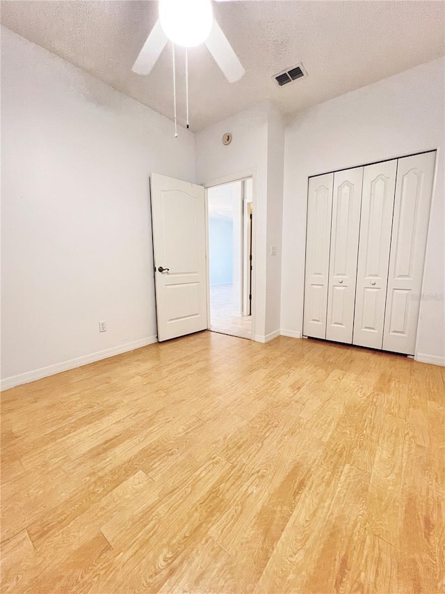 unfurnished bedroom with ceiling fan, a closet, light hardwood / wood-style flooring, and a textured ceiling