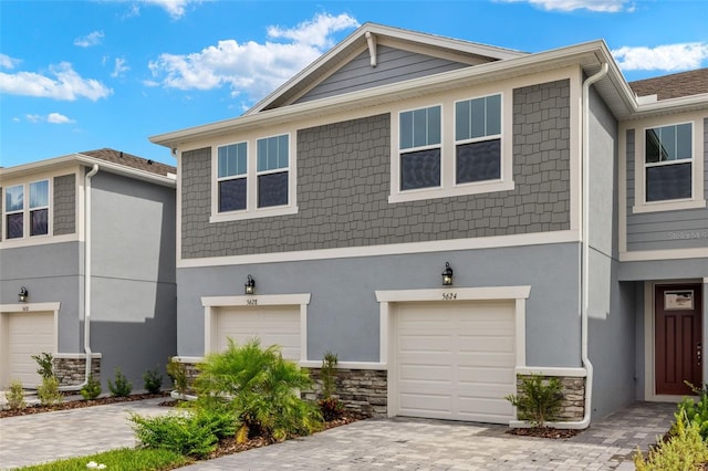 view of front facade featuring a garage, stone siding, decorative driveway, and stucco siding