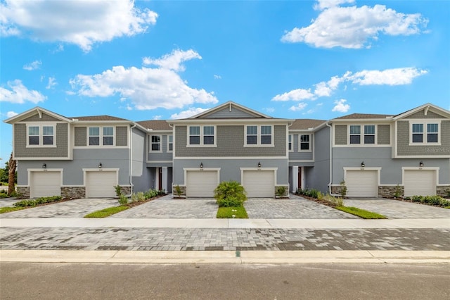 multi unit property with an attached garage, stone siding, decorative driveway, and stucco siding