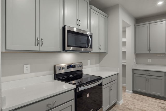 kitchen with appliances with stainless steel finishes, gray cabinets, light countertops, and light wood finished floors