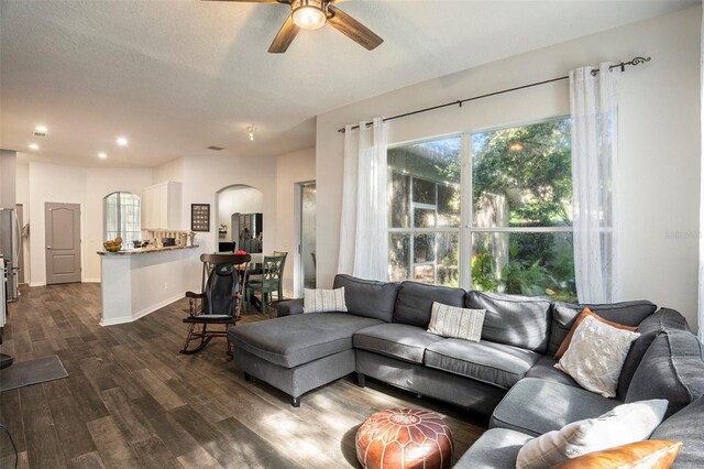 living room with a textured ceiling, ceiling fan, and dark hardwood / wood-style flooring