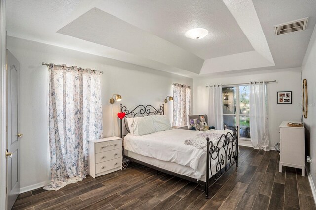 bedroom featuring a tray ceiling, dark wood-type flooring, and a textured ceiling