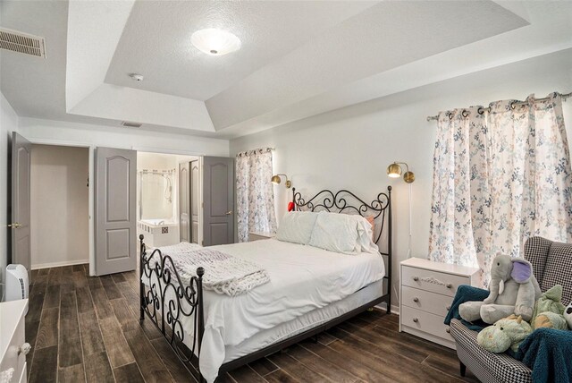 bedroom with ensuite bath, dark wood-type flooring, a textured ceiling, and a tray ceiling