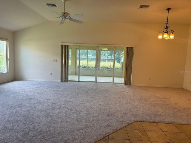 tiled spare room featuring ceiling fan with notable chandelier and vaulted ceiling