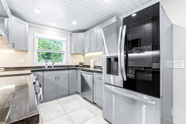 kitchen featuring light tile patterned floors, gray cabinets, appliances with stainless steel finishes, wooden ceiling, and dark stone counters