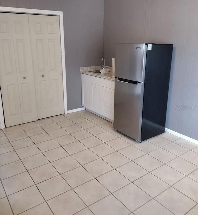 kitchen featuring stainless steel fridge, sink, light tile patterned flooring, and white cabinets