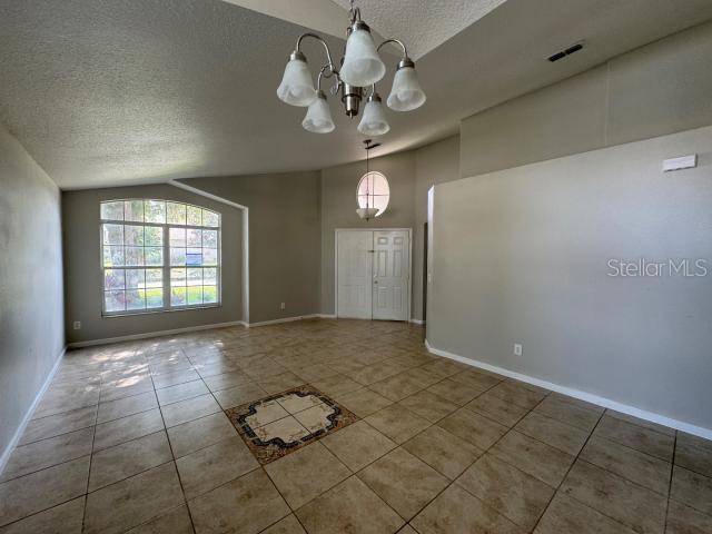 tiled spare room featuring a textured ceiling, vaulted ceiling, and an inviting chandelier