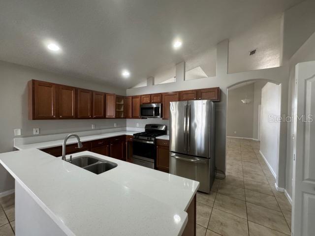 kitchen with sink, stainless steel appliances, lofted ceiling, and light tile patterned flooring