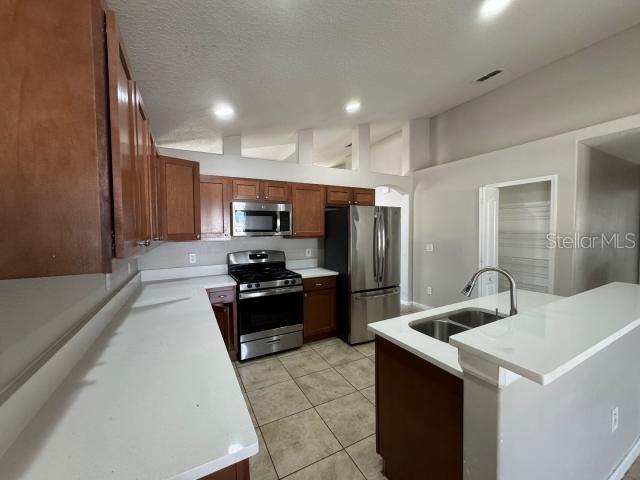 kitchen featuring sink, kitchen peninsula, a textured ceiling, light tile patterned flooring, and stainless steel appliances