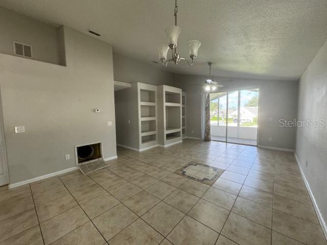 unfurnished room with light tile patterned flooring, ceiling fan with notable chandelier, and a textured ceiling