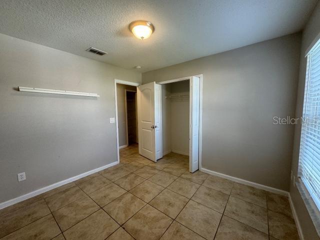 unfurnished bedroom featuring light tile patterned flooring, a textured ceiling, a closet, and multiple windows