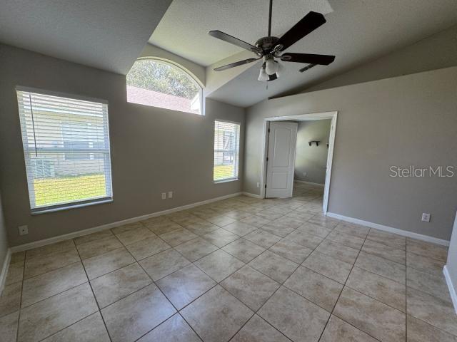 spare room with ceiling fan, vaulted ceiling, and light tile patterned floors