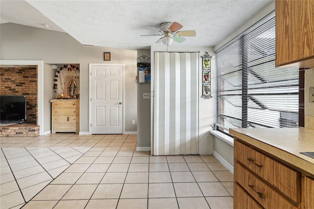 interior space featuring ceiling fan, vaulted ceiling, a textured ceiling, and light tile patterned floors