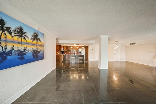 interior space featuring baseboards, visible vents, a textured ceiling, and ornate columns