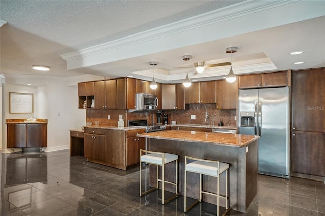 kitchen featuring a kitchen bar, ornamental molding, a tray ceiling, stainless steel appliances, and decorative backsplash