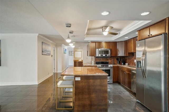 kitchen featuring ceiling fan, a center island, a raised ceiling, appliances with stainless steel finishes, and dark tile patterned flooring