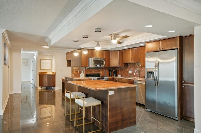 kitchen featuring a ceiling fan, a sink, a tray ceiling, appliances with stainless steel finishes, and decorative backsplash