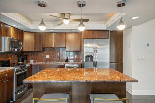 kitchen featuring ceiling fan, a tray ceiling, a breakfast bar, appliances with stainless steel finishes, and backsplash