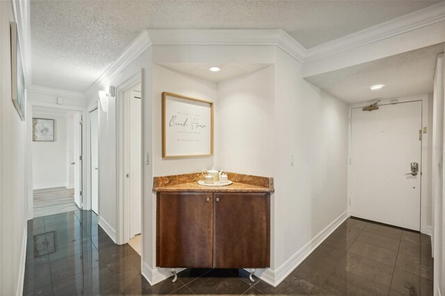 hall with dark tile patterned floors, ornamental molding, and a textured ceiling