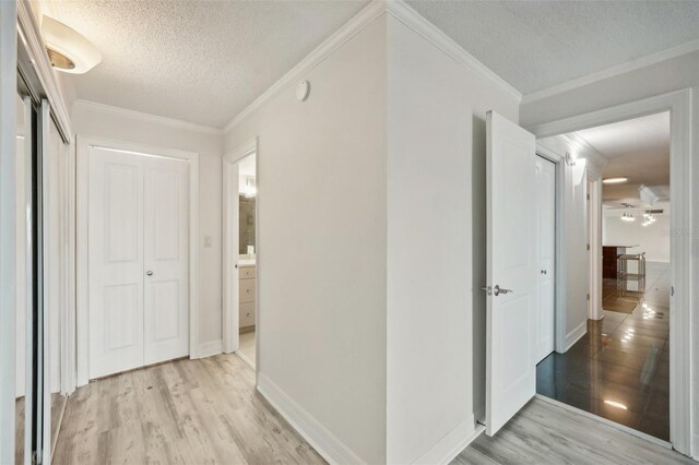 hallway with ornamental molding, light hardwood / wood-style flooring, and a textured ceiling