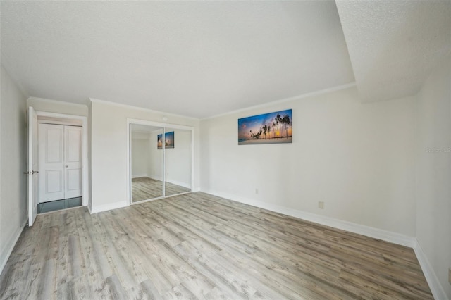 unfurnished bedroom with wood finished floors, baseboards, a closet, a textured ceiling, and crown molding