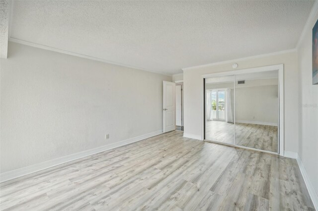 unfurnished bedroom featuring crown molding, light hardwood / wood-style flooring, a closet, and a textured ceiling