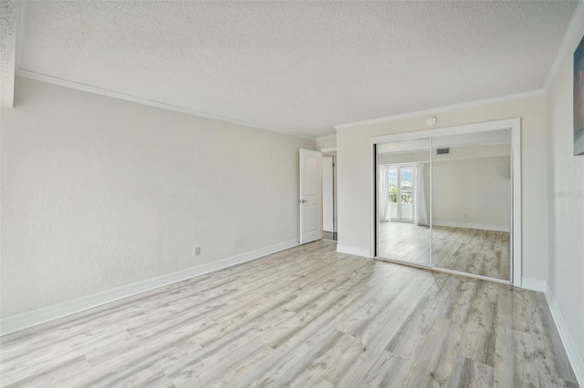 unfurnished bedroom with ornamental molding, a textured ceiling, a closet, light wood-style floors, and baseboards