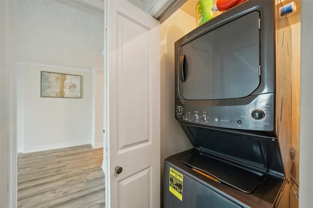 clothes washing area with stacked washer / dryer, crown molding, and light wood-type flooring