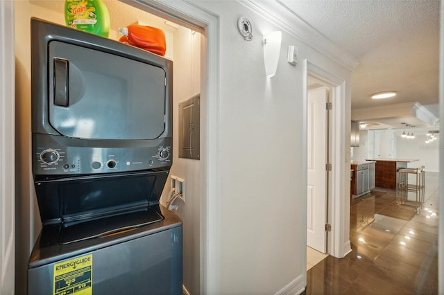 clothes washing area featuring tile patterned flooring, crown molding, stacked washer and dryer, electric panel, and laundry area