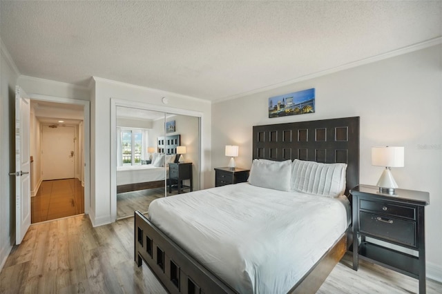 bedroom featuring a closet, light wood-style floors, crown molding, and a textured ceiling